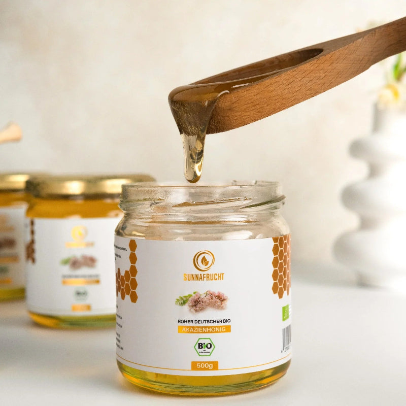 Glas Bio Akazienhonig, Deckel offen, Honig läuft von Holzlöffel, Naturprodukt