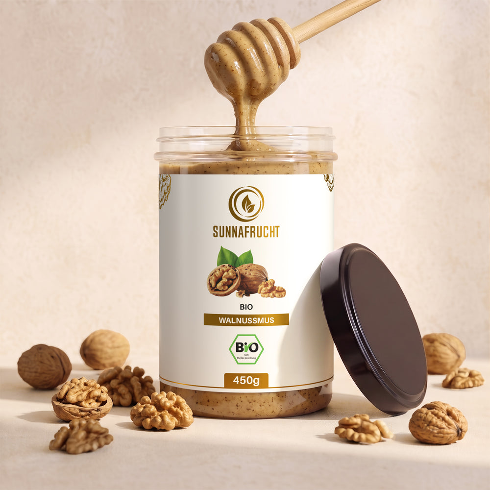 Geöffnetes Glas Bio-Walnussmus, das Mus läuft vom Honiglöffel zurück ins Glas, daneben ganze Walnüsse